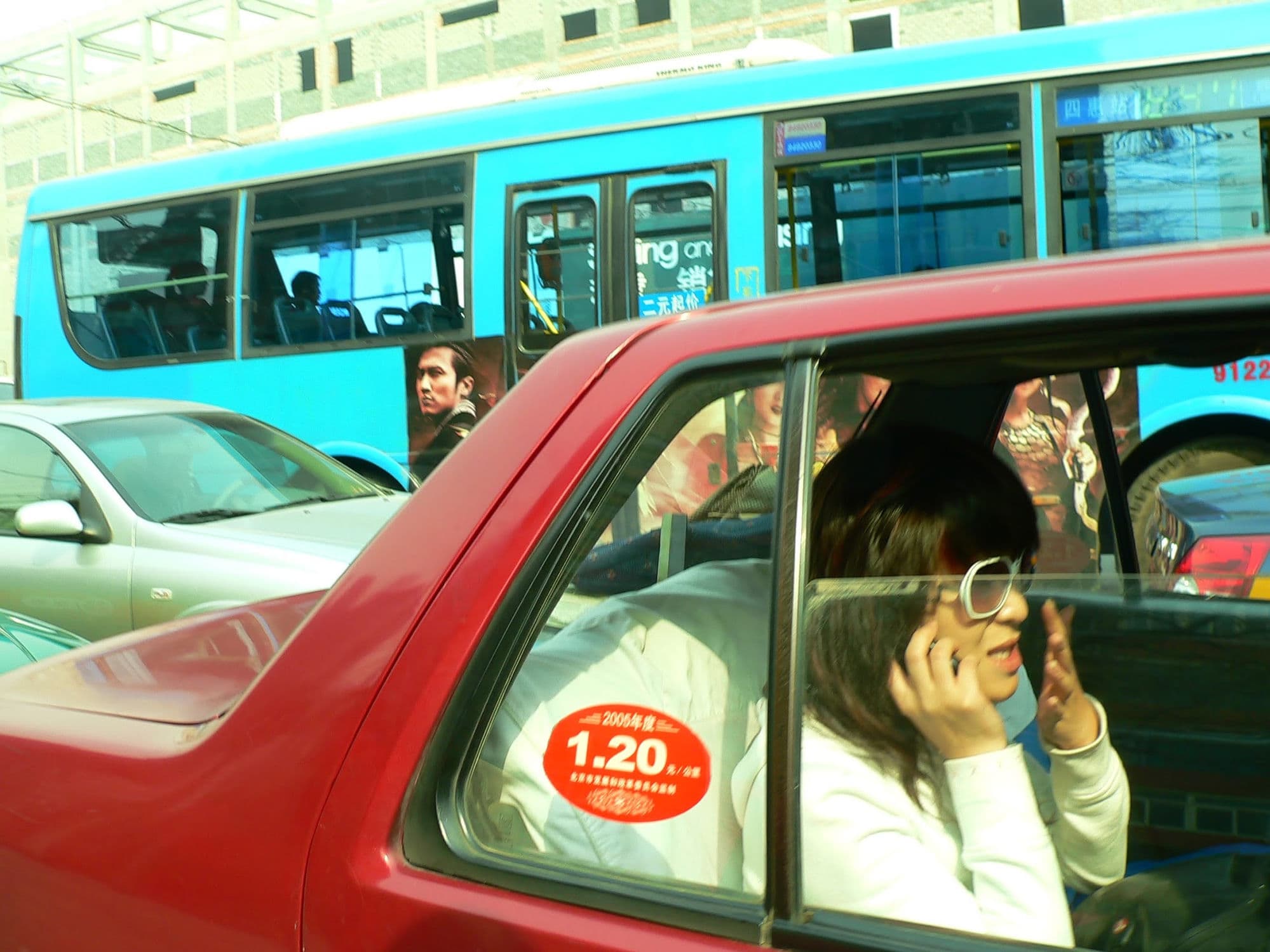 2005年北京,一辆红色北京出租车停在一辆蓝色公交车旁,后座上一个女人正在打电话。